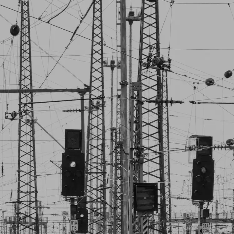 Emaranhado complexo de cabos elétricos, torres metálicas e sinais ferroviários contra um céu pálido. Atmosfera industrial fria e opressiva.