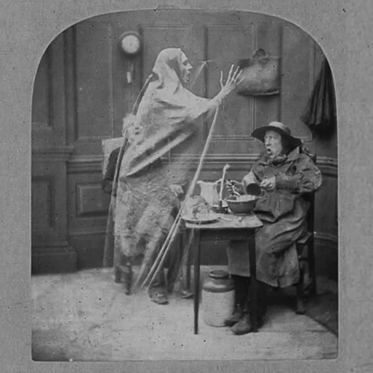 Foto antiga estilo vitoriano. Um vulto espectral e translúcido paira sobre um homem sentado à mesa, que reage com expressão de choque.