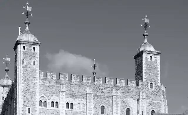 Torre de Londres: Muralhas e torres de pedra branca com cata-ventos sob céu limpo. Fotografia P&B de um dos locais mais assombrados da Inglaterra.