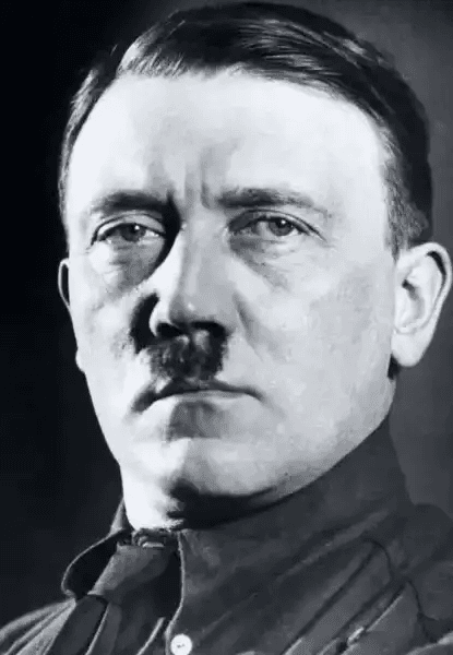 Retrato em preto e branco de Adolf Hitler, líder da Alemanha nazista. Ele aparece de frente, com expressão severa e olhar penetrante, cabelos penteados para o lado e bigode característico. Veste uniforme militar escuro com gola alta e botão visível. O fundo é neutro e escuro, destacando seu rosto como foco central da composição.