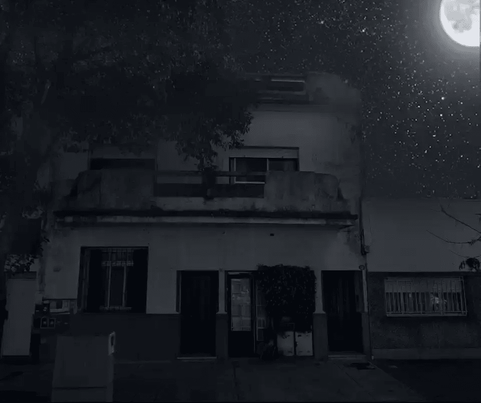 Casa de dois andares em Saavedra sob um céu noturno surreal com lua cheia e estrelas pontilhadas. A iluminação sombria destaca a sacada e as janelas escuras.
