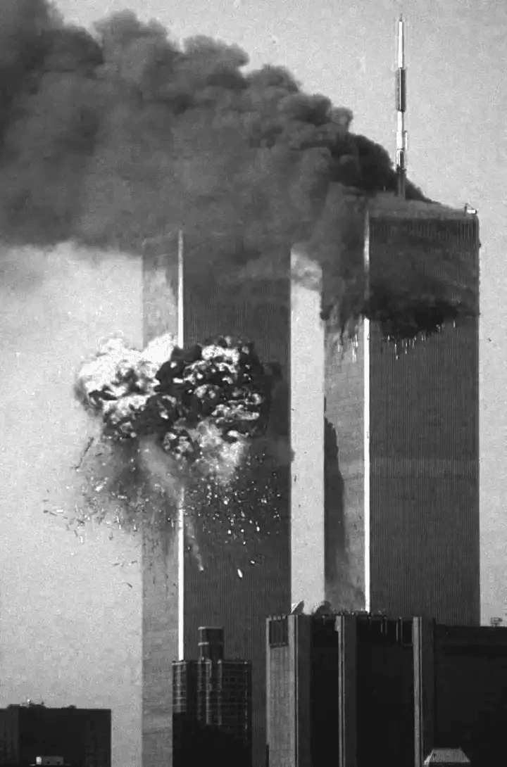 Fotografia histórica do 11 de setembro. Uma explosão massiva irrompe da segunda torre do World Trade Center, enquanto a primeira já exala uma densa nuvem de fumaça negra contra o céu.