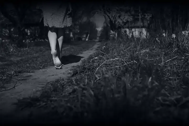 Caminhada Solitária: Pés descalços caminhando por trilha de terra em jardim sob luz sombria. Cena em preto e branco que sugere mistério, isolamento e uma jornada silenciosa.